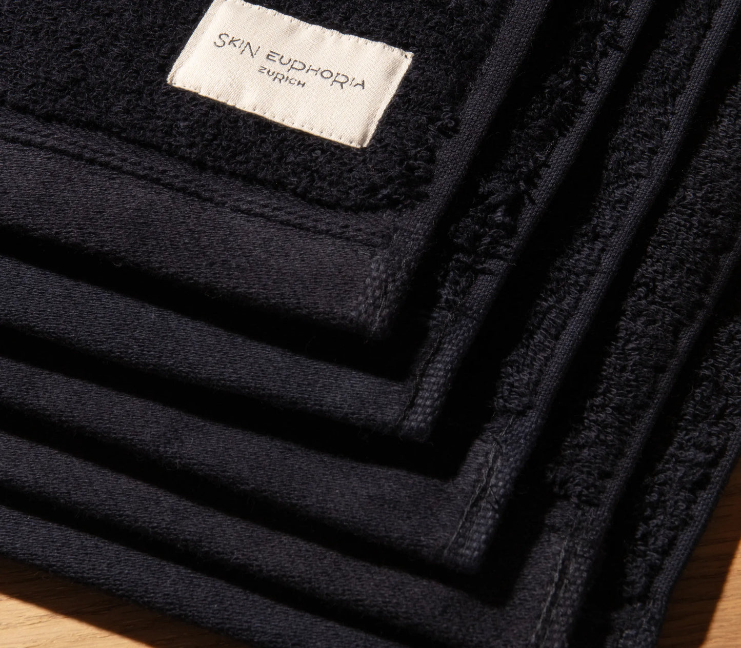 Black towel with 'Skin Euphoria Zurich' label on a wooden surface