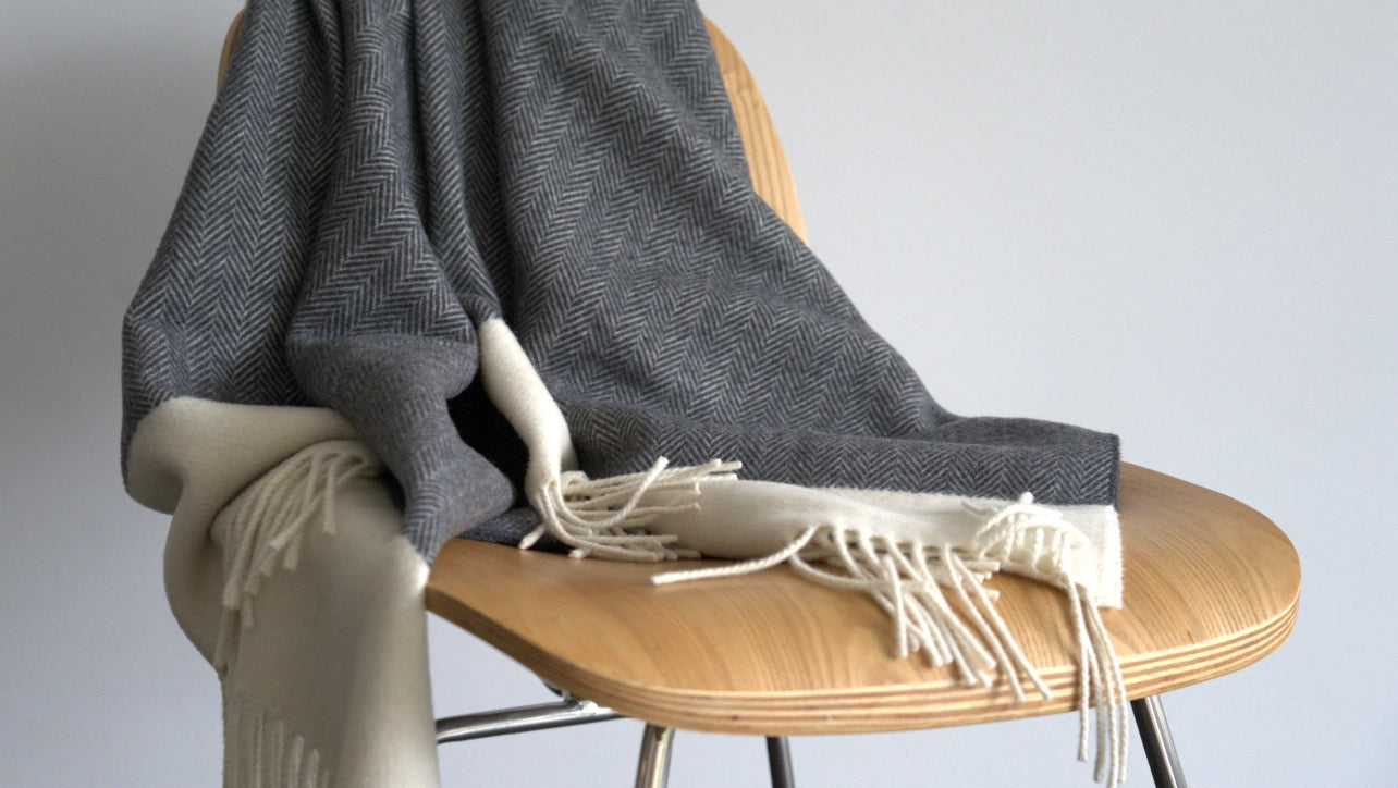 Gray blanket with white fringe draped over a wooden chair against a plain background