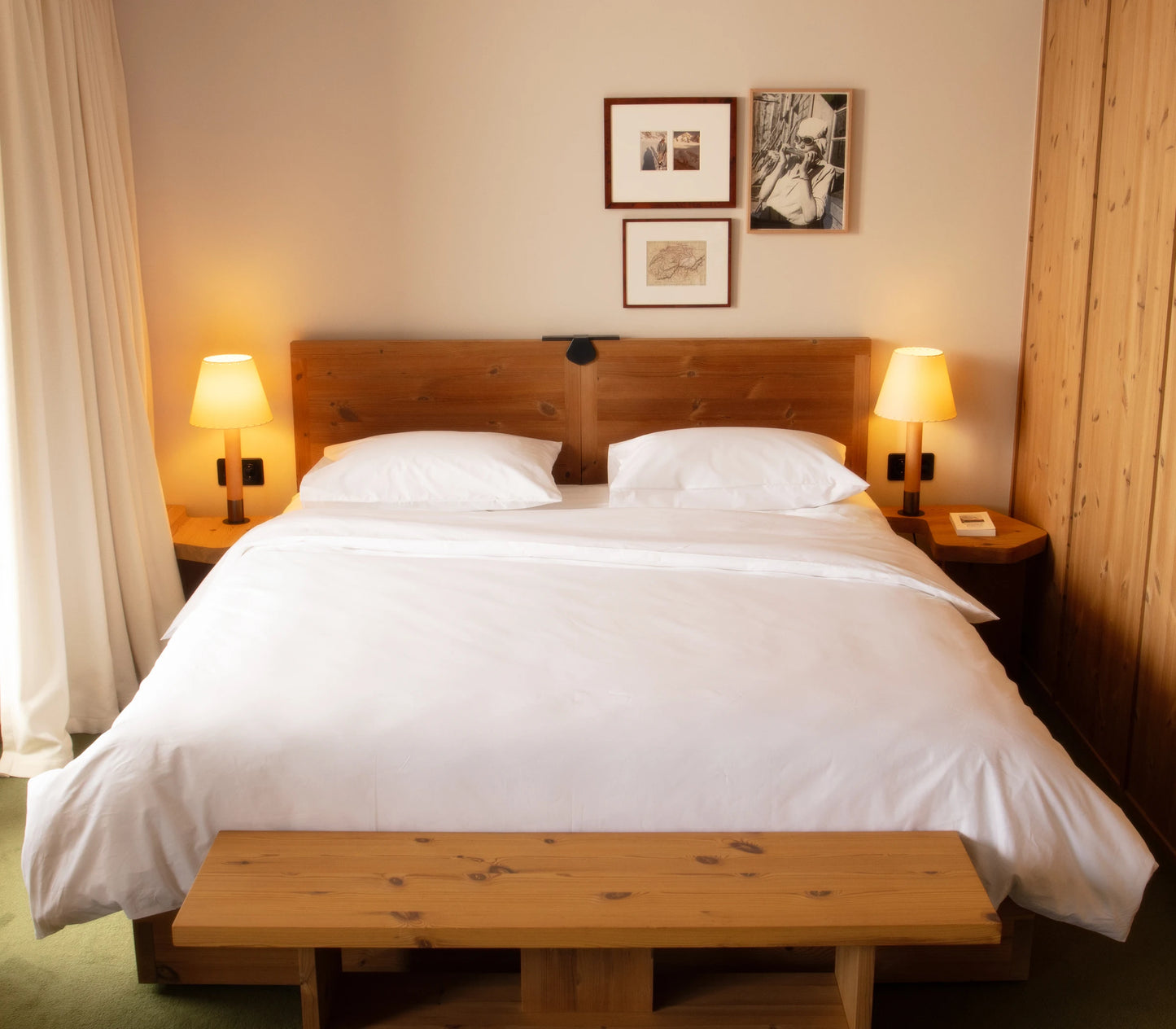 Bedroom with wooden bed and bench, lamps, and framed pictures on the wall.