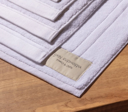 White bath mat with 'Skin Euphoria' label on a wooden surface