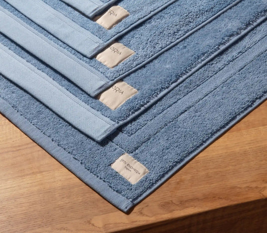 Set of blue bath mats with a brand label on a wooden surface