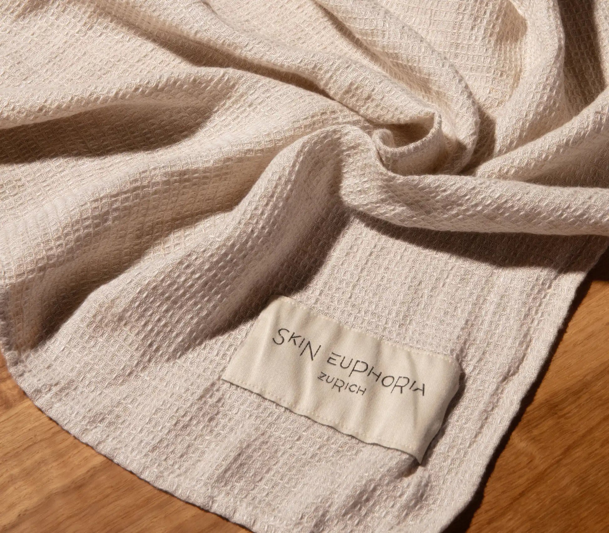 Close-up of a textured beige towel with 'SKIN EUPHORIA ZURICH' label on a wooden surface
