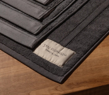 Black bath mat with 'SKIN EUPHORIA' label on a wooden surface