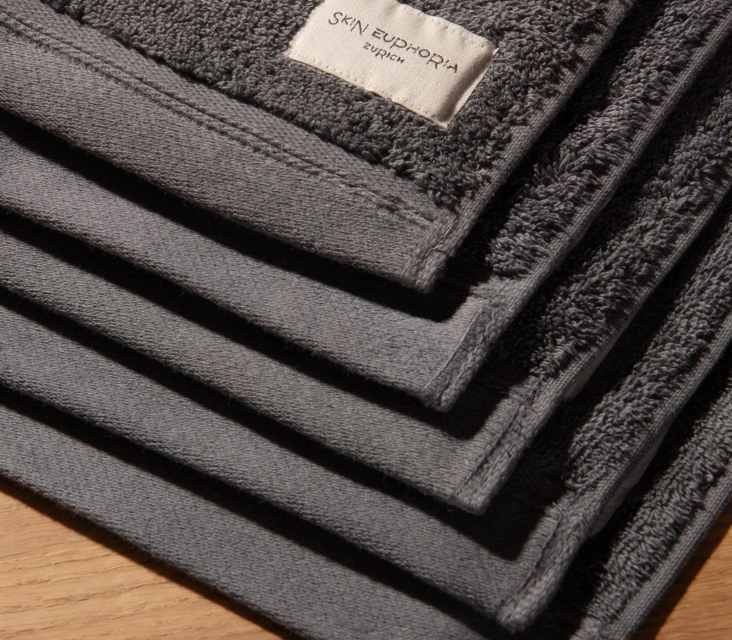 Stack of dark gray towels with a brand label on a wooden surface