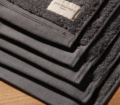 Stack of dark gray towels with a brand label on a wooden surface