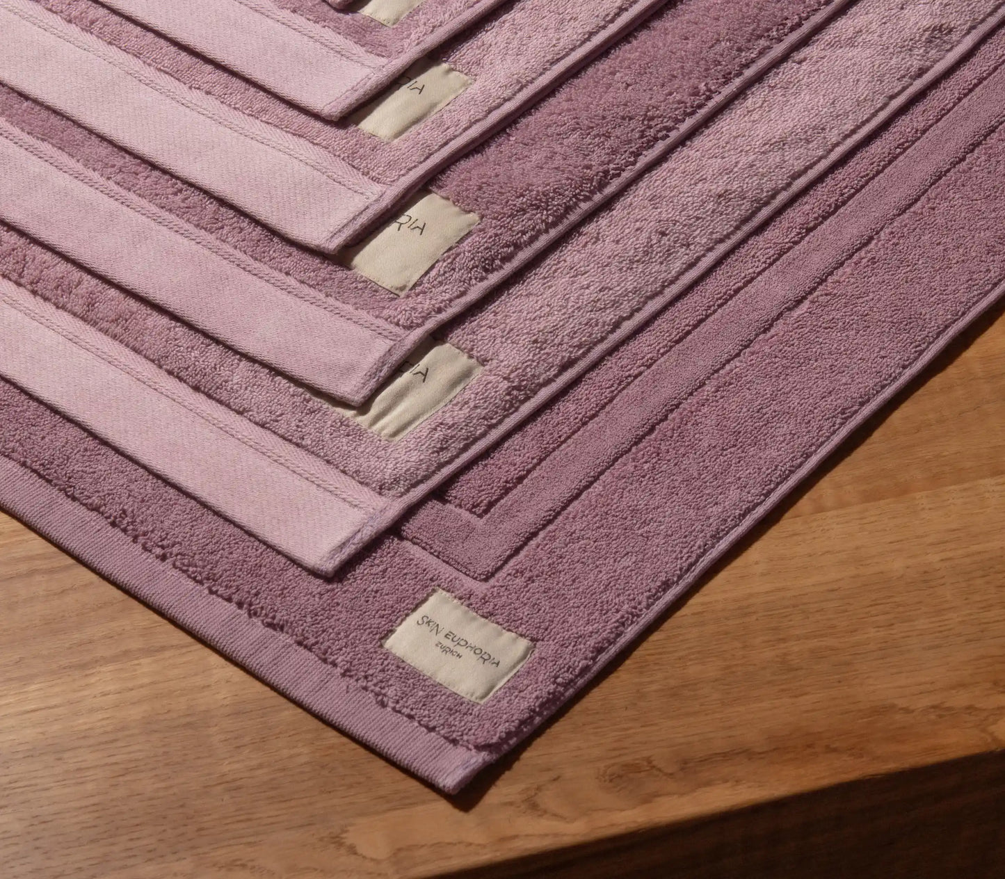Set of pink bath mats with a brand label on a wooden surface