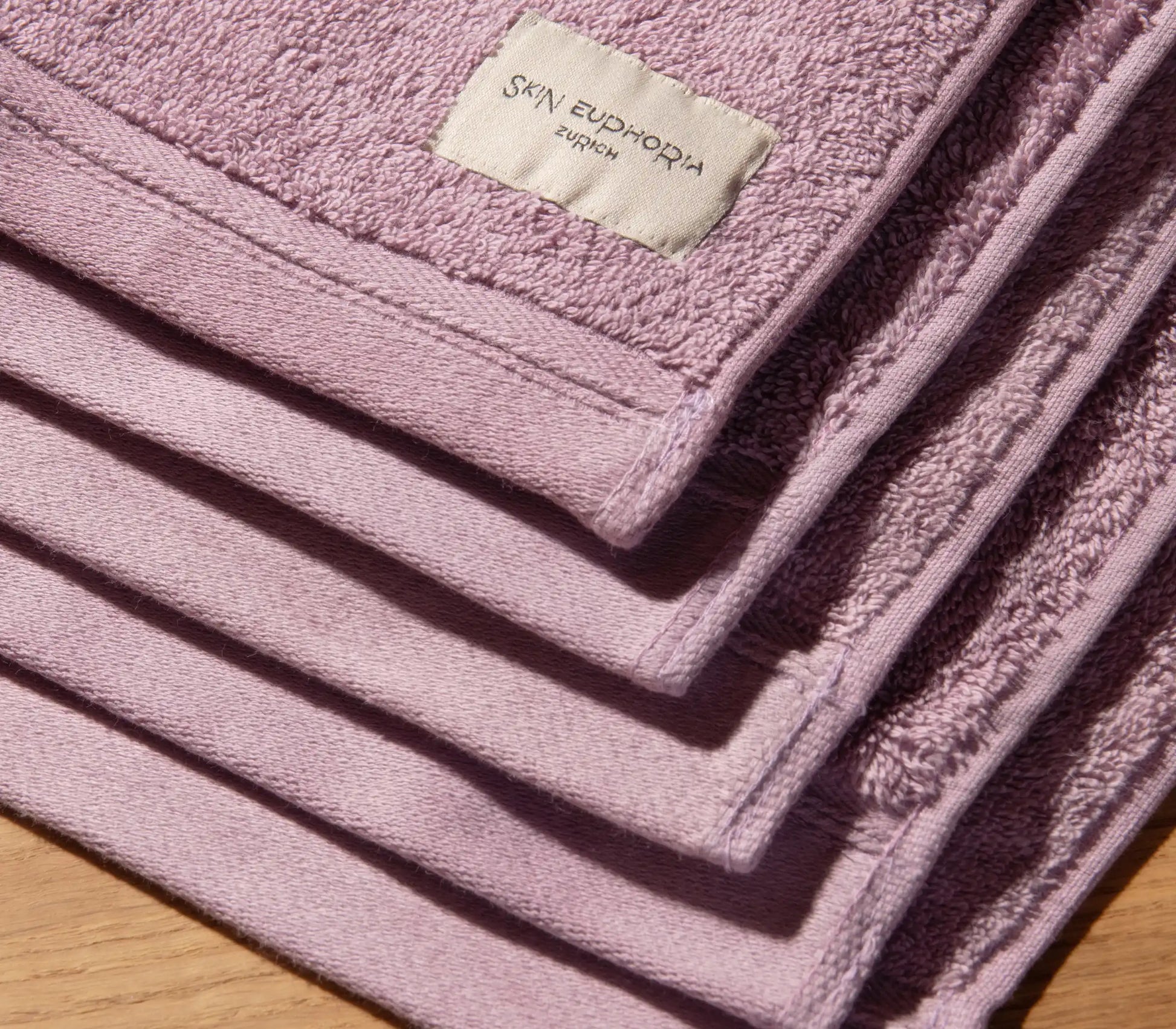 Stack of pink towels with a brand label on a wooden surface
