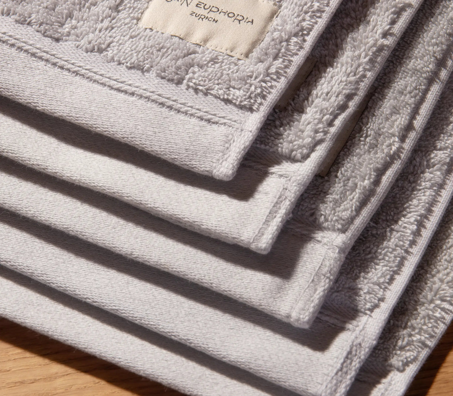 Stack of gray towels with a brand label on a wooden surface