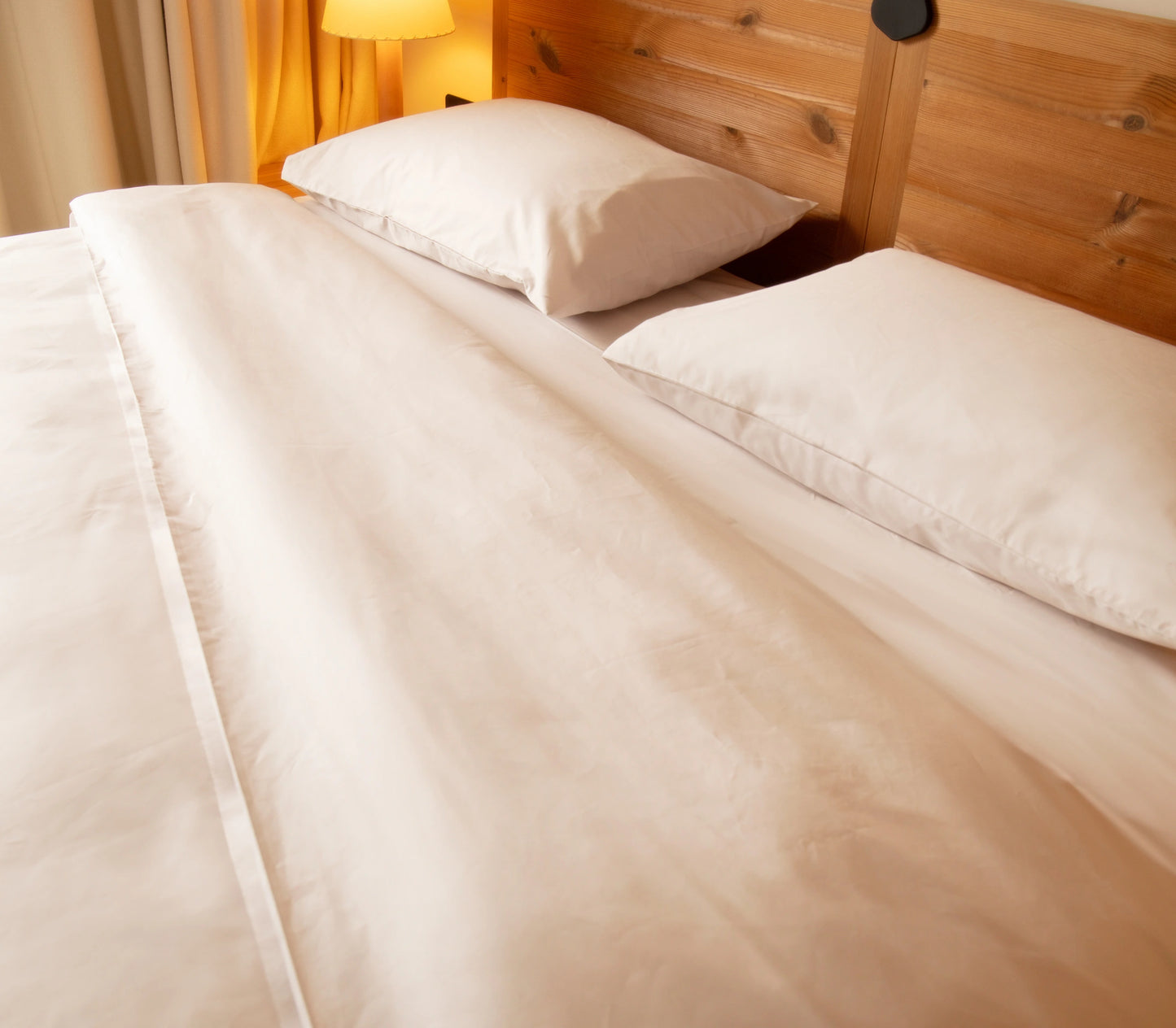 Neatly made bed with white bedding and pillows in a bedroom setting.