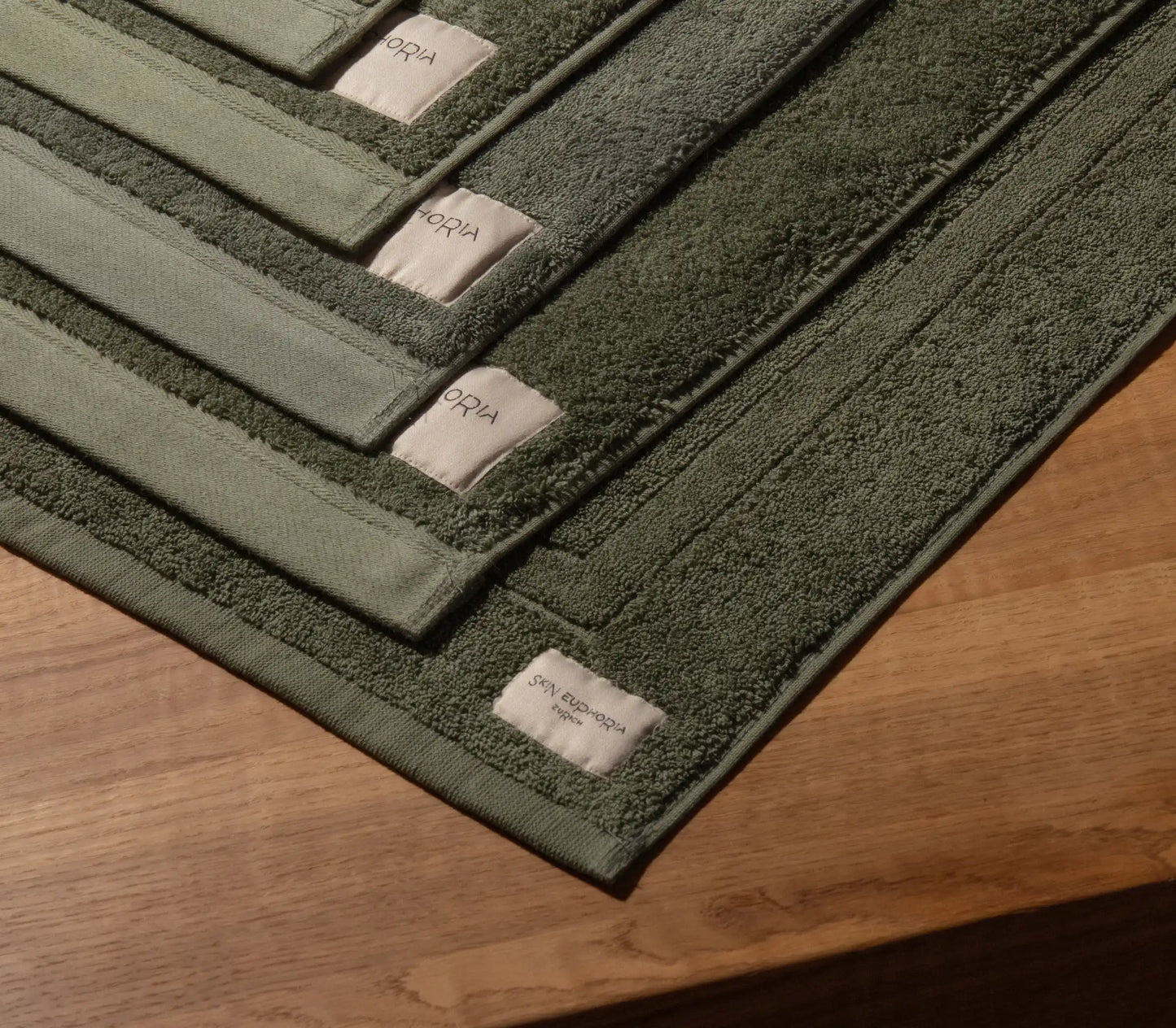 Set of green bath mats with brand labels on a wooden floor