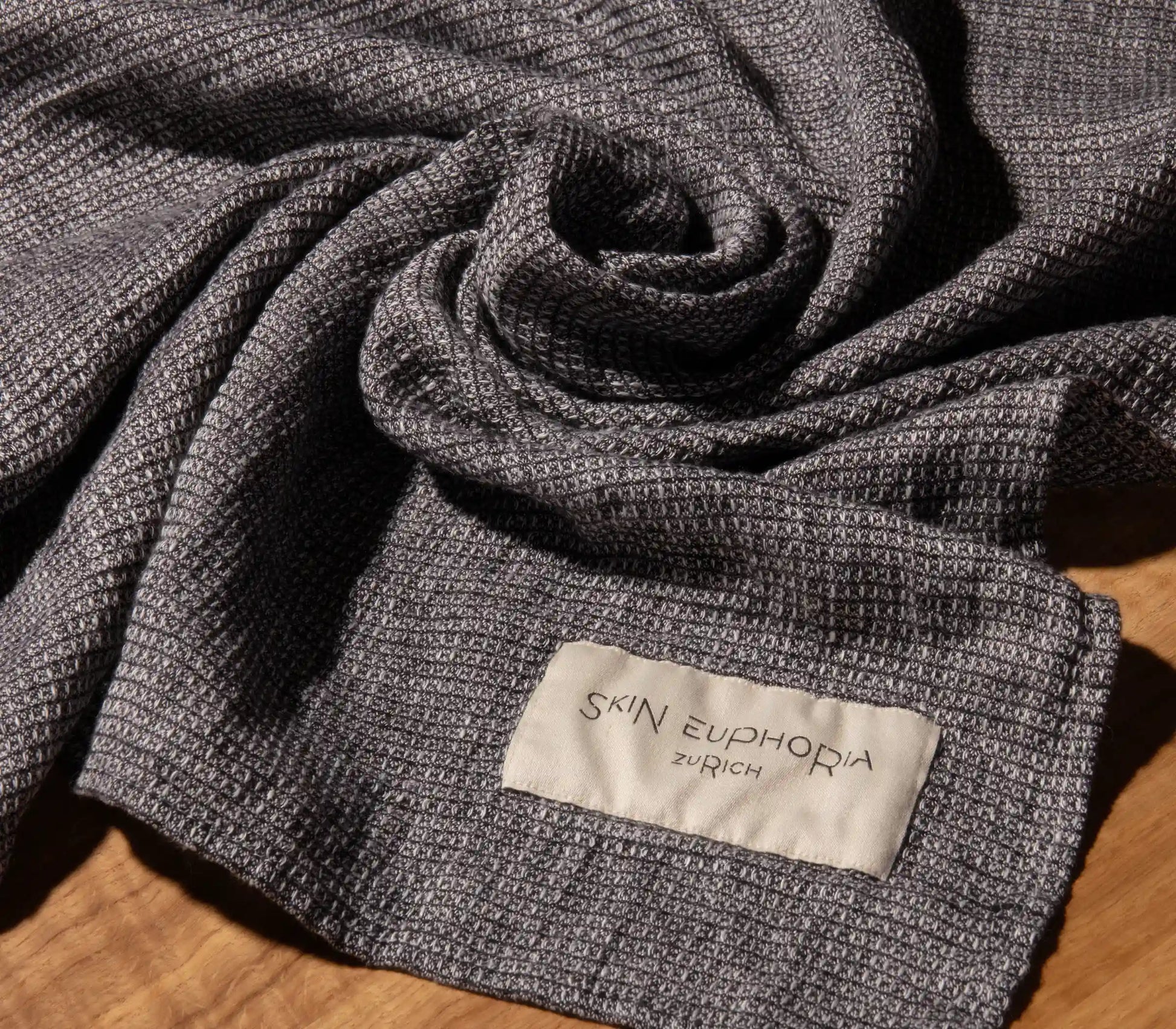 Textured gray fabric with 'Skin Euphoria Zurich' label on a wooden surface