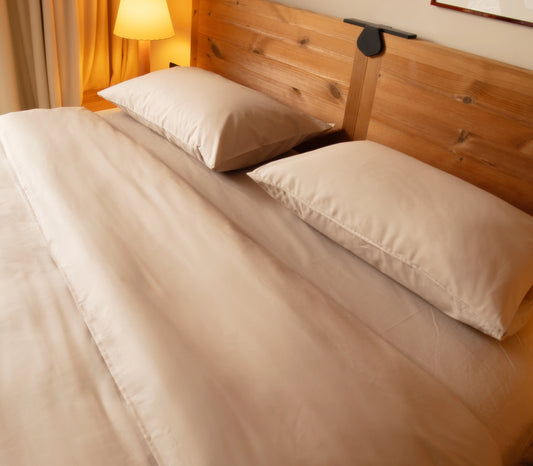 Bed with beige bedding and wooden headboard in a warm-lit room