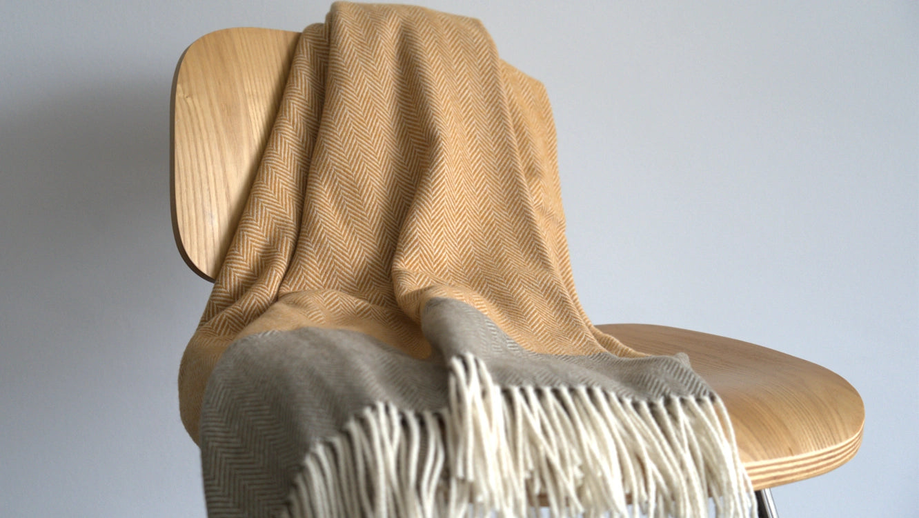 Beige blanket with white fringe draped over a wooden chair against a plain background