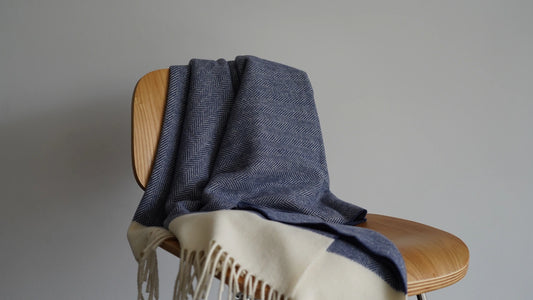 Blue woven blanket draped over a wooden chair with a plain background