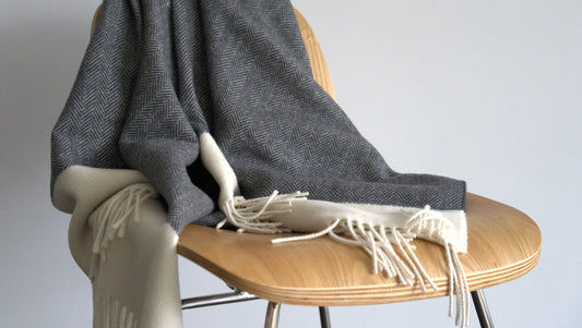 Gray blanket with white fringe draped over a wooden chair against a plain background