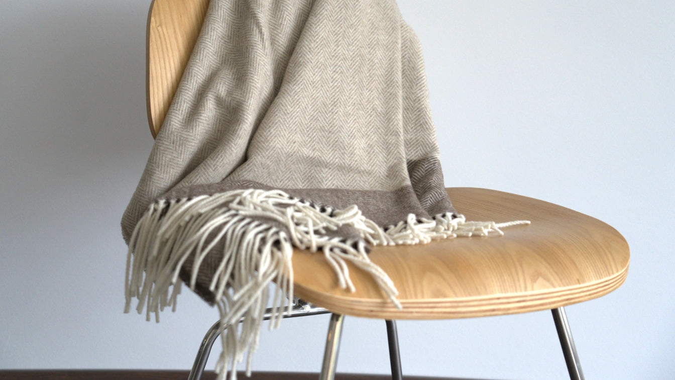 Wooden chair with a gray blanket draped over it against a plain background